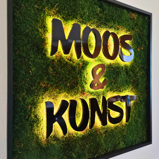 Moosbild mit Flachmoos und 3D Buchstaben rückleuchtend. Nachtansicht mit leuchtenden Buchstaben sichtbar.  Gesamtansicht 1x1 Meter. Handgefertigter Holzbilderrahmen lackiert. Logo rückleuchtend. Individuelle Leuchtreklame. Geschenkidee.