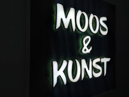 Moosbild mit Flachmoos und 3D Buchstaben front- und rückleuchtend. Nachtansicht mit leuchtenden Buchstaben sichtbar.  Gesamtansicht 1x1 Meter. Handgefertigter Holzbilderrahmen lackiert. Logo front- und rückleuchtend. Individuelle Leuchtreklame.