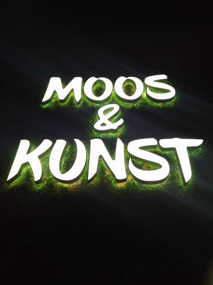 Moosbild mit Flachmoos und 3D Buchstaben front- und rückleuchtend. Nachtansicht mit leuchtenden Buchstaben sichtbar.  Gesamtansicht 1x1 Meter. Handgefertigter Holzbilderrahmen lackiert. Logo front- und rückleuchtend. Individuelle Leuchtreklame.