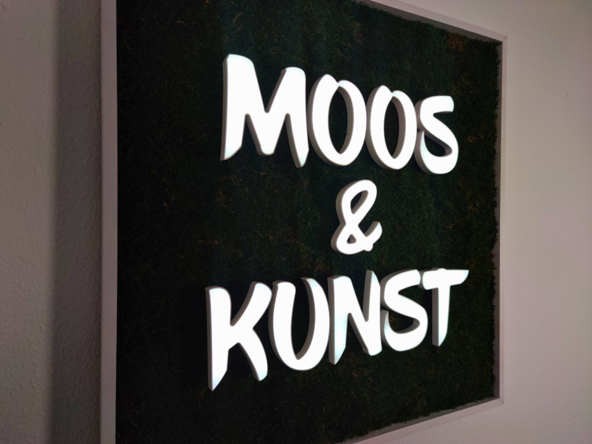 Moosbild mit Flachmoos und 3D Buchstaben frontleuchtend. Nachtansicht mit leuchtenden Buchstaben sichtbar.  Gesamtansicht 1x1 Meter. Handgefertigter Holzbilderrahmen lackiert. Logo Frontleuchtend. Individuelle Leuchtreklame. Geschenkidee.