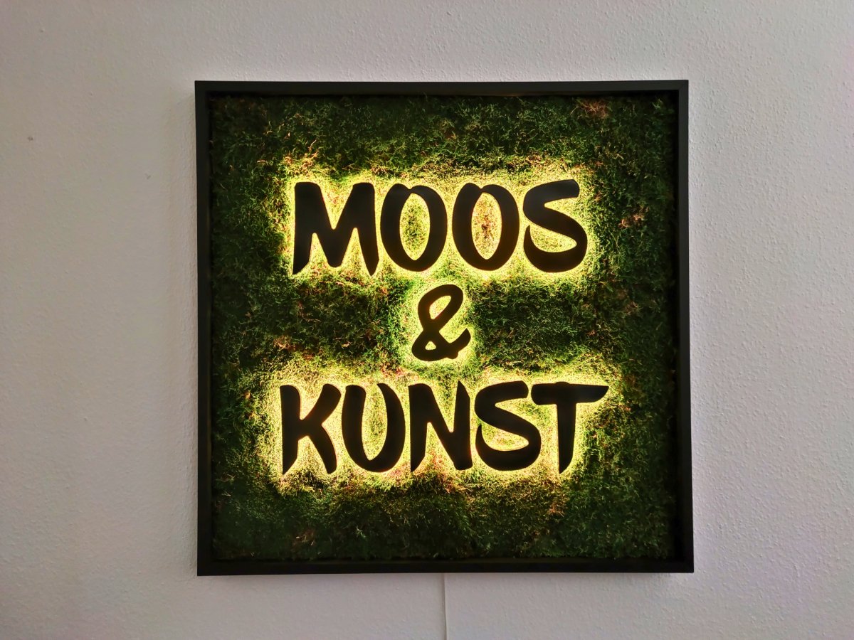 Moosbild mit Flachmoos und 3D Buchstaben rückleuchtend. Nachtansicht mit leuchtenden Buchstaben sichtbar.  Gesamtansicht 1x1 Meter. Handgefertigter Holzbilderrahmen lackiert. Logo rückleuchtend. Individuelle Leuchtreklame. Geschenkidee.