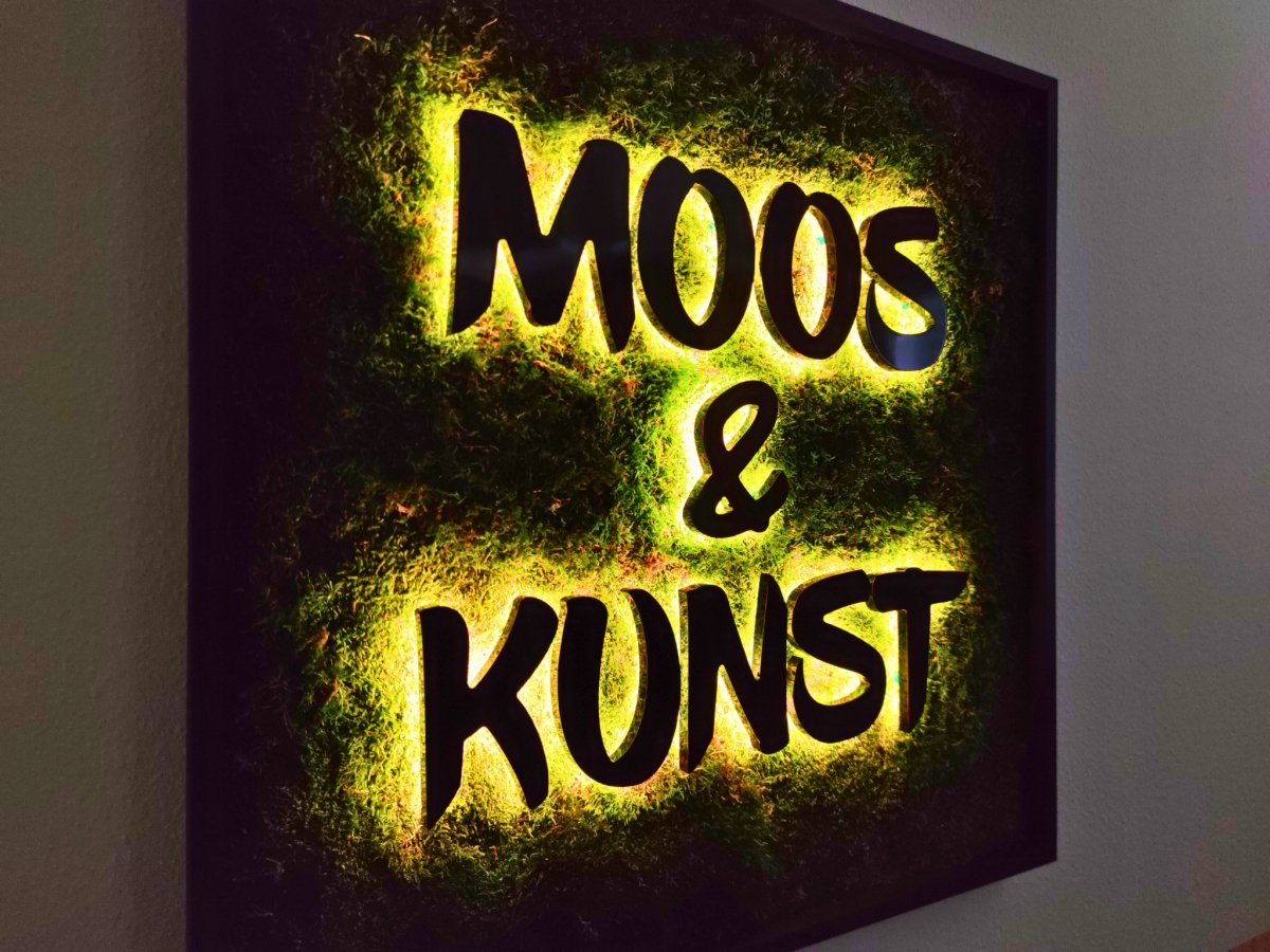 Moosbild mit Flachmoos und 3D Buchstaben rückleuchtend. Nachtansicht mit leuchtenden Buchstaben sichtbar.  Gesamtansicht 1x1 Meter. Handgefertigter Holzbilderrahmen lackiert. Logo rückleuchtend. Individuelle Leuchtreklame. Geschenkidee.